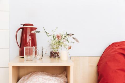 Geburtshilfe, Detail im Wehenzimmer: Regal neben dem Bett mit bunten Kissen, Teekanne und Gläsern und Arrangement von Blüten und Zweigen